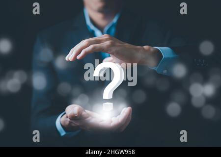 Ask question online concept, Businessman hand hold interface question marks sign web, Question marks drawn on black background. Concept of searching f Stock Photo