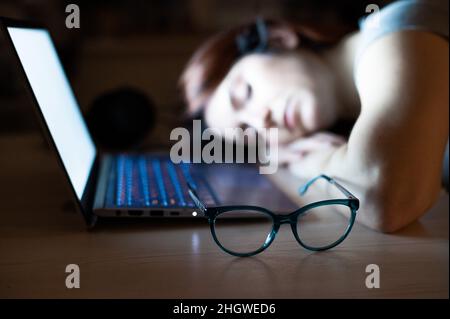 The exhausted employee worked overtime and fell asleep at his desk. Deadline Work at night with a laptop. The student is preparing for the exam. Stock Photo