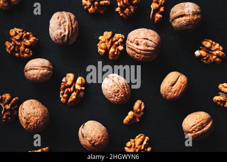 Whole and peeled walnuts on a black background. Close-up, flat lay, top view. Food background, selective focus. Stock Photo