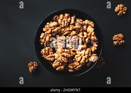 Peeled walnuts in a black bowl on a black background. Close-up, flat lay, top view. Food background, selective focus. Stock Photo