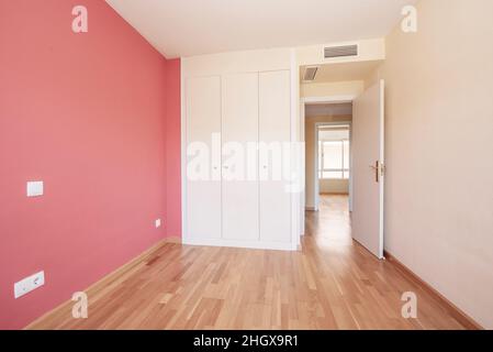 Room with white built-in wardrobe with three bodies, pastel red wall and wooden floors Stock Photo