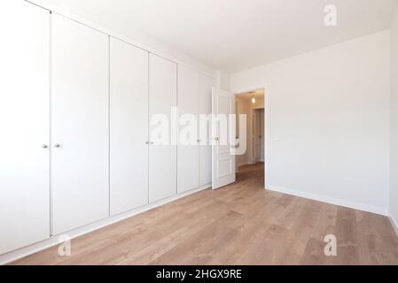 empty room with built-in wardrobe with white doors covering the entire wall and light wooden floors Stock Photo
