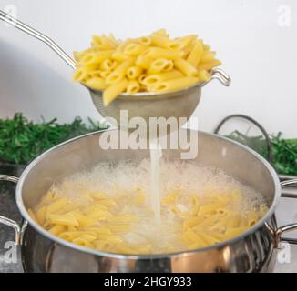 Cooking Pasta pour the penne pasta into a metal pot of boiling water. Boiled penne on a steel colander, in a cooking class. Stock Photo