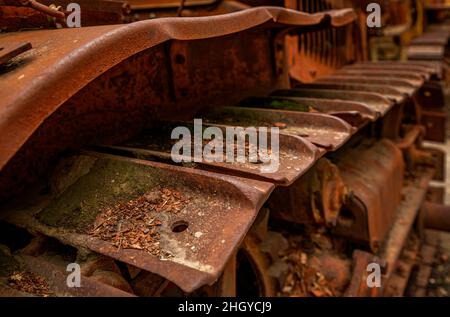 Old rusty tread of abandoned heavy equipment, a tractor, with fallen leaves and moss on the rusted tread Stock Photo