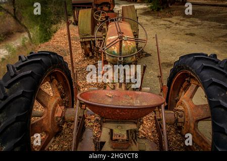 Old and rusty abandoned heavy equipment, tractor, amongst trees with fallen yellow leaves on the ground Stock Photo