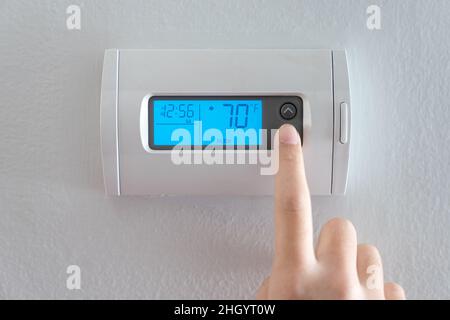 Hand press indoor room thermostat to lower the temp Stock Photo
