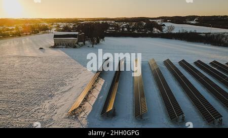 Solar panels being lit up by the setting sun in the winter landscape. Fresh snow covers the land. Stock Photo