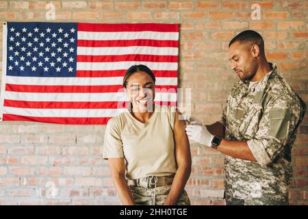 Cheerful female soldier smiling happily after getting vaccinated in the military hospital. American servicewoman having a medical adhesive applied to Stock Photo