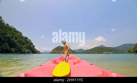 Man with sunglasses and hat rows pink plastic canoe along sea ag Stock Photo