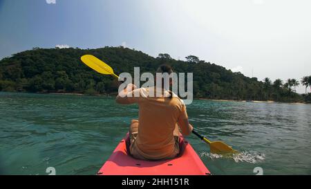 Man with sunglasses and hat rows pink plastic canoe along sea ag Stock Photo