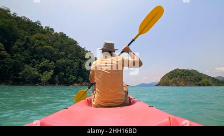 Man with sunglasses and hat rows pink plastic canoe along sea ag Stock Photo