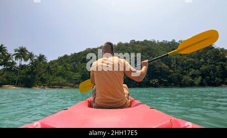 Man with sunglasses and hat rows pink plastic canoe along sea ag Stock Photo