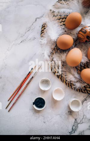 Top view eggs, white feathers, brushes, paints on marble background. Stock Photo