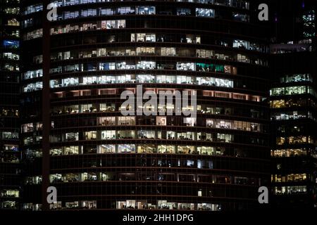 Modern office building with big windows at night view close up view, in windows glowing light shines and some people inside, Singapore. Stock Photo