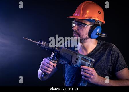 A young man in overalls protective helmet hard hat hold electric drill. Stock Photo