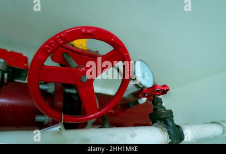 Red hand wheel of main supply water piping in the fire extinguishing system and white water supply pipe. Fire sprinkler system with red pipes hanging Stock Photo