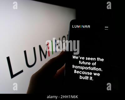 Person holding smartphone with website of US lidar company Luminar Technologies Inc. on screen in front of logo. Focus on center of phone display. Stock Photo