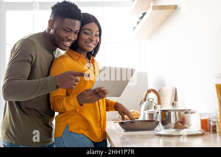 Happy Black Couple Using Digital Tablet While Cooking Food Together In Kitchen Stock Photo