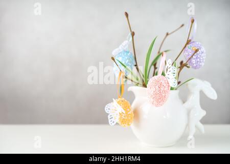 Home interior with easter decor. Vase with willow tree branches with Easter eggs and bunny on white table and background with copy space Stock Photo