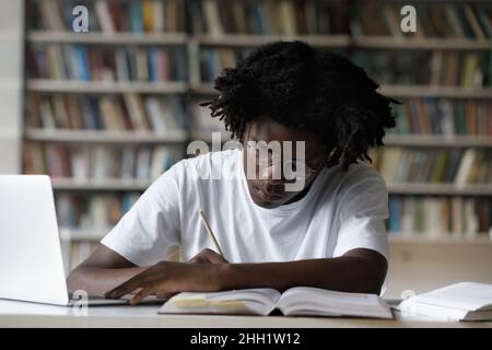 Focused fresh gen Z Black college student writing notes Stock Photo