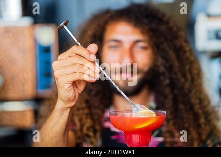 Handsome smiling curly hair bartender preparing cocktail at the resort bar Stock Photo