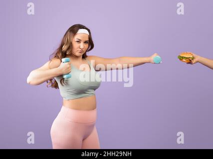 Serious caucasian pretty plus size young woman in sportswear lifting up dumbbell