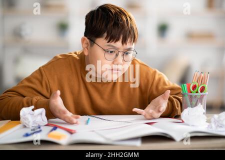 Furious asian kid looking at exercise book and gesturing Stock Photo