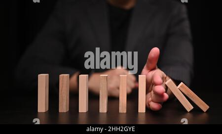 Businessman hand trying to stop dominoes. Protection finance from domino effect concept. Stock Photo