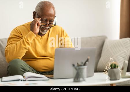 Senior African Man Squinting Eyes Using Laptop Wearing Eyeglasses Indoor Stock Photo
