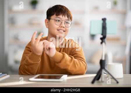 Cute asian teen boy vlogger streaming from home, using cellphone Stock Photo