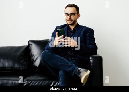 Focused young guy spend time on couch use ecommerce software on mobile telephone check email in convenient client app. Stock Photo