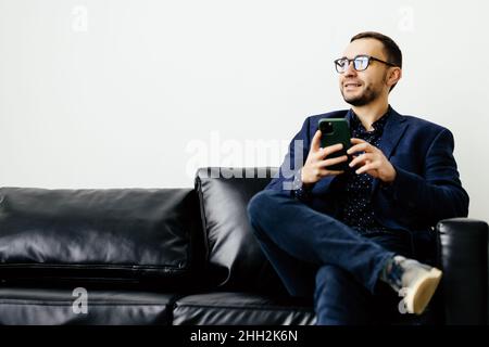 Focused young guy spend time on couch use ecommerce software on mobile telephone check email in convenient client app. Stock Photo