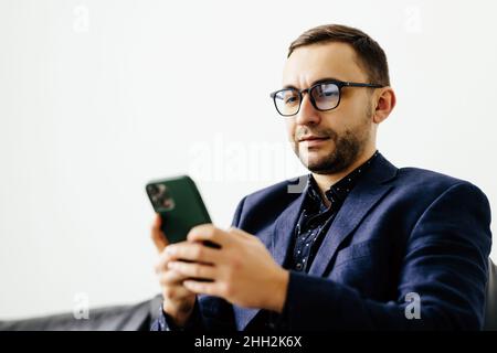 Focused young guy spend time on couch use ecommerce software on mobile telephone check email in convenient client app. Stock Photo
