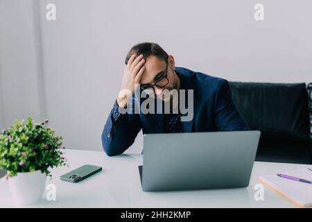 Frustrated businessman sitting on desk with hand on head in office Stock Photo