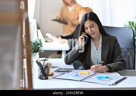 Beautiful businesswoman talking on mobile phone and putting signature on business document. Stock Photo