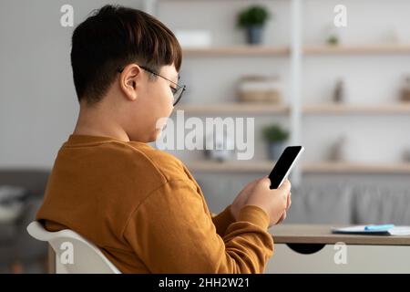 Overweight asian teenager sitting at table and using smartphone Stock Photo
