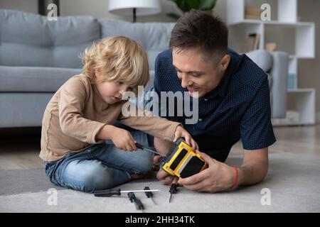 Funny adorable small boy fixing toy with caring father. Stock Photo