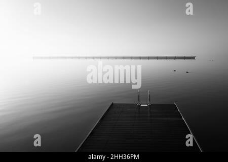 Dawn on a wooden jetty stretching into the silent ocean in stunning black and white Stock Photo