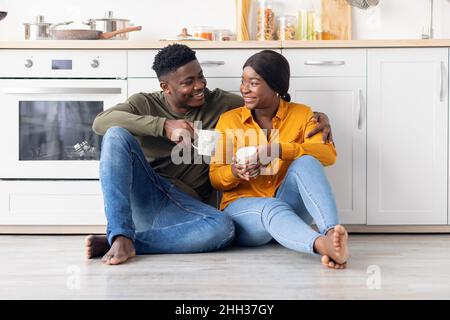 Romantic Black Millennial Couple Relaxing With Coffee In Kitchen, Sitting On Floor Stock Photo