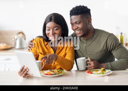 Happy Black Spouses Eating Breakfast Together And Using Digital Tablet In Kitchen Stock Photo