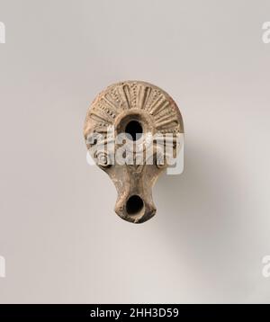 Terracotta oil lamp 1st century B.C.–1st century A.D. Greek or Roman Mold-made. Central filling hole within a small, concave discus, surrounded by a circular band. Broad sloping shoulder, decorated with a pattern of radiating ridges (elongated leaves?) interspersed with lines of dots; a raised knob on left edge; two spirals flanking sides of nozzle, with heart-shaped leaf on top and angular sides to wick hole. Raised base ring, and slightly concave base.Intact.. Terracotta oil lamp. Greek or Roman. 1st century B.C.–1st century A.D.. Terracotta. Hellenistic or Early Imperial. Terracottas Stock Photo