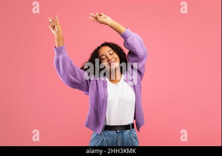 Portarit of excited young black lady dancing, celebrating success or victory on pink studio background Stock Photo