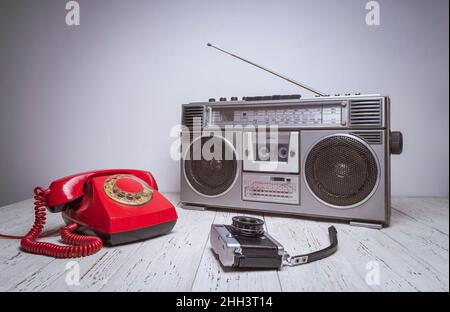 An old retro tape recorder, telephone and camera are on a wooden table. Vintage filtered old style photo.