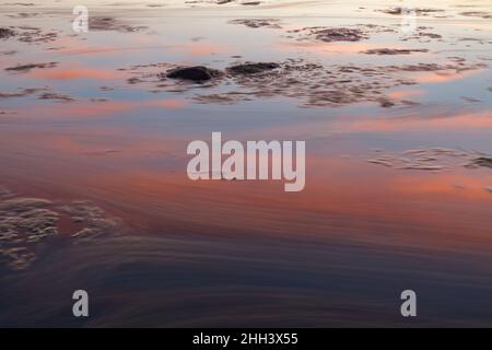 Sunset with a beutiful pink colored clouds. Long exposure photo of rocky sea shore in the evening Stock Photo