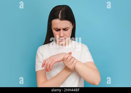 Young female massaging hand suffering from joint pain, isolated on blue background wall. Girl having rheumatoid arthritis. Woman touching wrist feelin Stock Photo