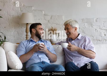 Cheerful senior 70s dad and adult grownup son drinking tea Stock Photo