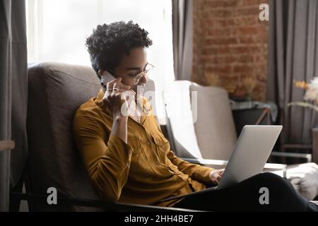 Positive busy African freelance employee woman sitting on couch Stock Photo