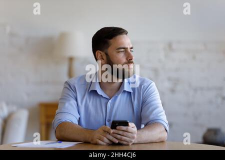 Thoughtful pensive millennial smartphone user man looking away Stock Photo