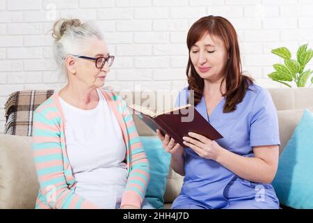 Woman reading a book to a senior citizen woman in nursing home Stock Photo