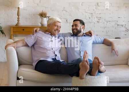 Cheerful retired father and grownup adult relaxing on comfortable couch Stock Photo